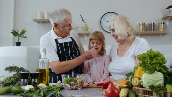 Senior Couple Grandmother and Grandfather in Kitchen Feeding Granddaughter Child with Chopped Pepper