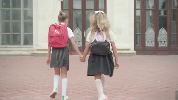 Back View of Cheerful Girls Running To School in the Morning. Wide Shot of Happy Caucasian