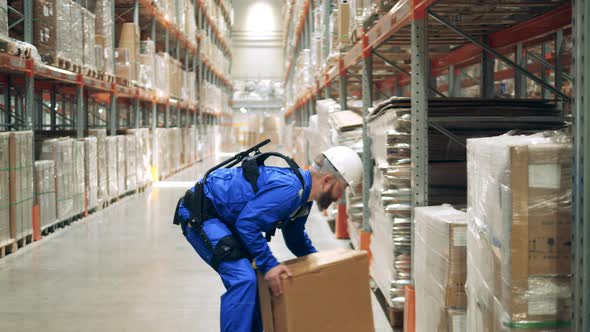 Storehouse Employee is Wearing Ergoskeleton and Lifting a Box