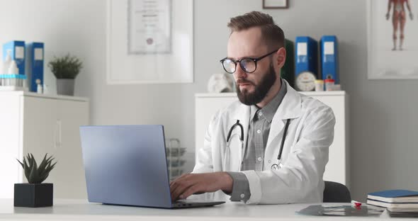 Young Male Doctor Working on Laptop in Clinic Office