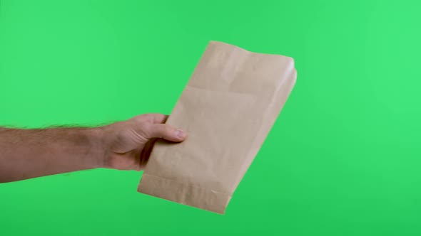 A Man's Hand Gives a Paper Shopping Bag to a Woman's Hand Against the Background of a Green Screen