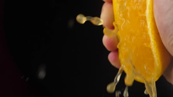 Hand squeezing orange slow motion on black background