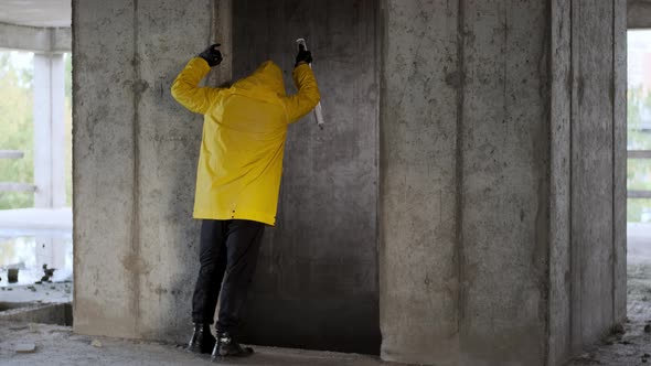 Inspection of Old Abandoned Unfinished Building By Man in Yellow Overalls and Flashlight