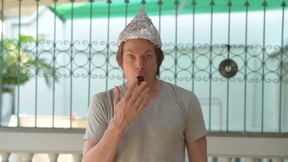 Young Man Wearing Tin Foil Hat and Looking Shocked Outdoors