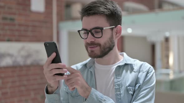 Portrait of Cheerful Young Male Designer Using Smartphone