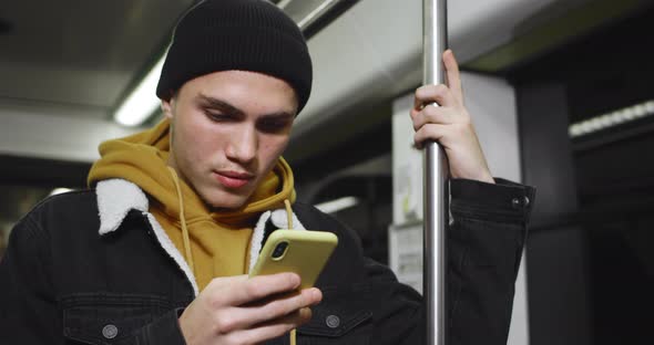 Young Handsome Student Using Smartphone and Smiling While Commuting on Public Transport. Millennial