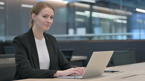 Businesswoman Smiling at Camera While Working on Laptop