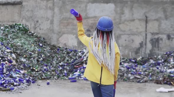 Woman in Hard Hat Standing Against the Pile of Broken Glass Used Bottles Next to the Wall