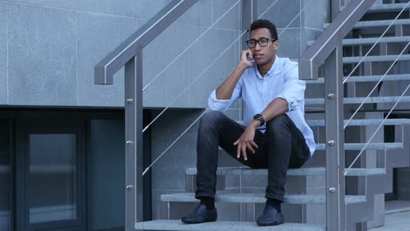 Young Black Man Sitting on Stairs and Talking on Phone