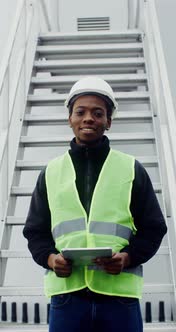 A Man in Work Uniform Smiles Looking at the Camera Standing Near a Wind Turbine