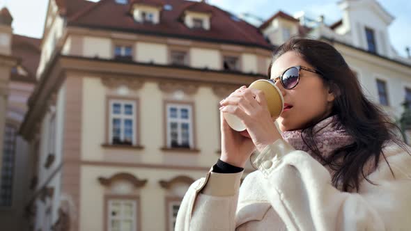 Smiling Beautiful Woman Drinking Hot Beverage Paper Cup Vintage Building in Background Low Angle