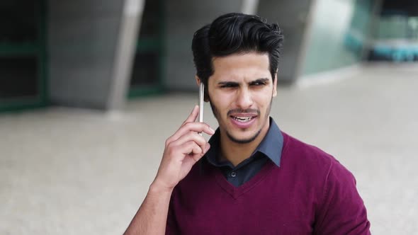 Handsome Young Man Talking on Phone Outside, Looking Serious