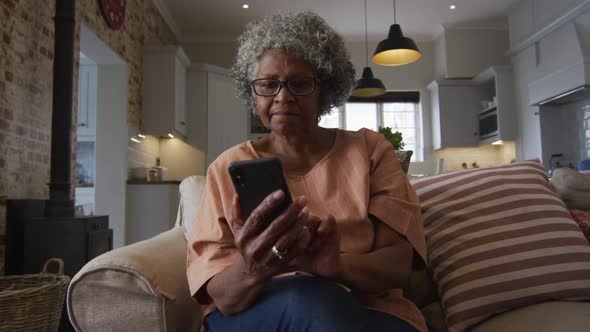 Senior african american woman using smartphone while drinking coffee while sitting on the couch at h