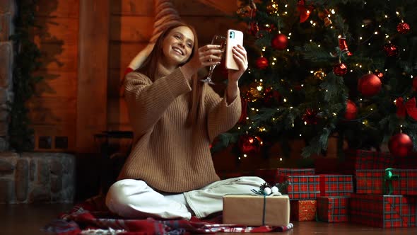Smiling Redhead Young Woman Clinking Glass of Champagne with Screen of Phone During Video Call
