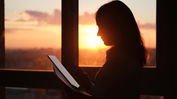 Girl Holding a Digital Tablet in Her Hands and Touching Her Fingers Indoors at Sunset