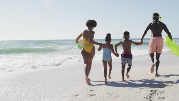 Smiling african american family holding hands and running on sunny beach