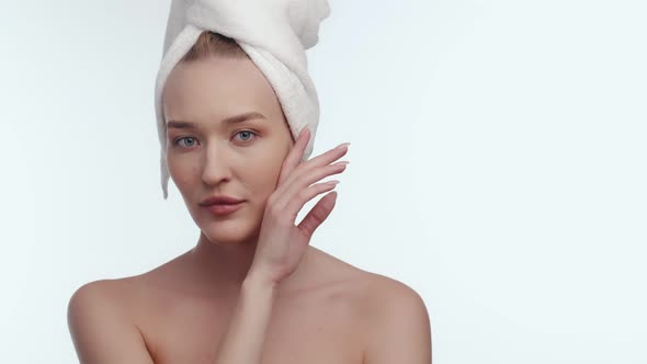 Attractive Woman with Towel on Head After Spa Looks Into Camera and Runs Hand Along Chin Front View