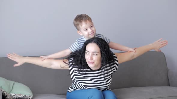 Happy Healthy Family Young Mom Lifting Cute Little Child Son Up Playing Plane on Sofa at Home, Funny