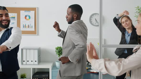 Playful AfroAmerican Businessman Dancing with Employees in Office Having Fun