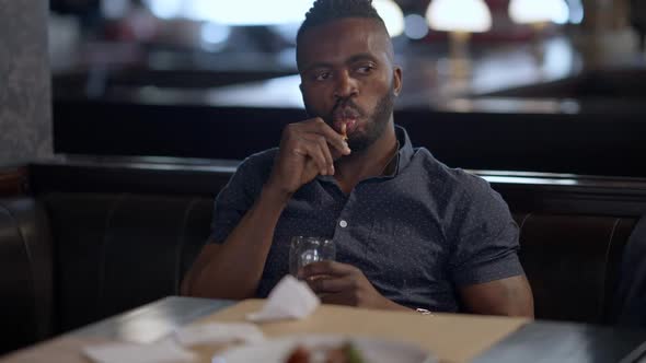 Handsome Relaxed Confident African American Man Eating Roasted Chicken Legs Sitting with Beer in