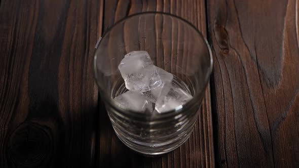 Top View of an Empty Glass with Falling Ice Cubes on a Brown Wooden Background