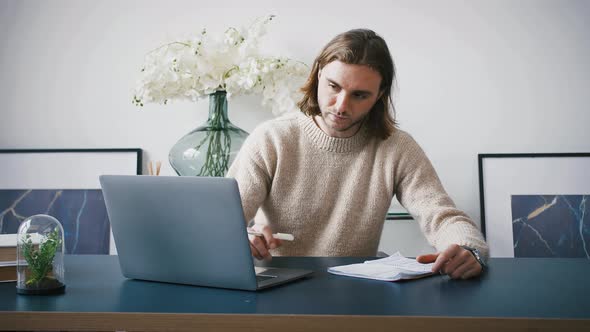 Young Man Employee is Looking Focused Typing on Laptop and Writing Down Info in Copybook While