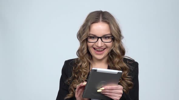 Pensive Businesswoman Texting on Her Tablet with Smile on Gray Background in Studio, Slow Motion