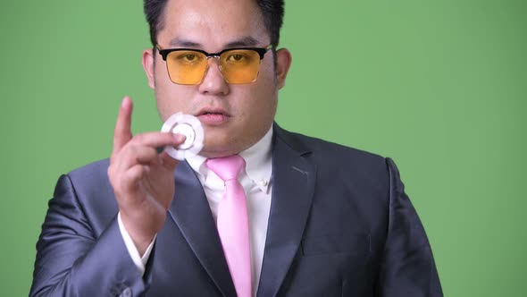 Young Handsome Overweight Asian Businessman Against Green Background