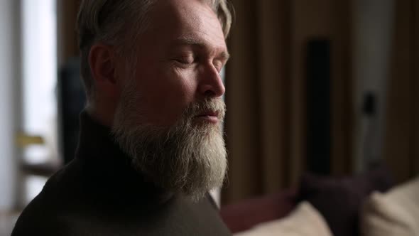 The face of an adult gray-haired man with a beard enjoying a cookie