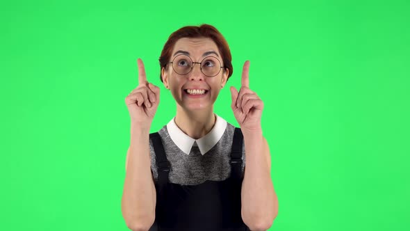 Portrait of Funny Girl in Round Glasses Is Pointing Up Fingers. Green Screen