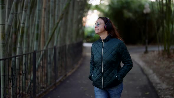 Carefree Woman in Casual Style is Walking in Park and Enjoying Music By Headphones