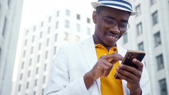 Black man in suit with hat types on smartphone