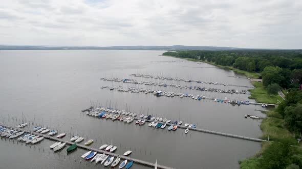 Full Sailboat harbor with white boats at a large lake next to forests.