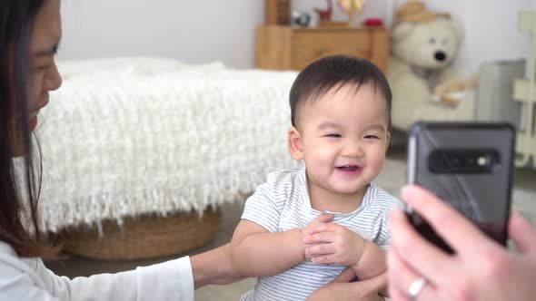 Infant Asian Boy with Mother Watching Video on Smartphone and Laughing