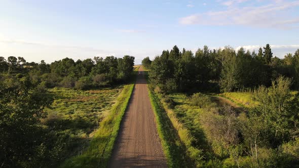 4k drone footage of car driving towards and underneath camera drone on red dirt road between lush gr