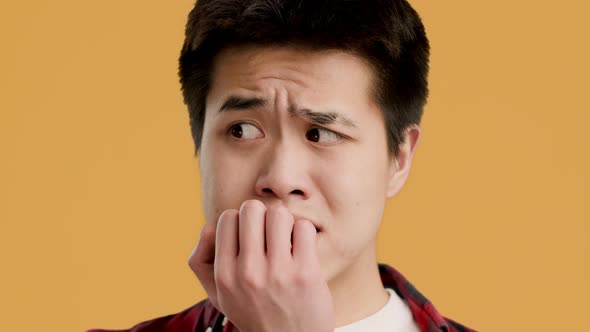Anxious Asian Guy Biting Nails Worrying About Something Yellow Background