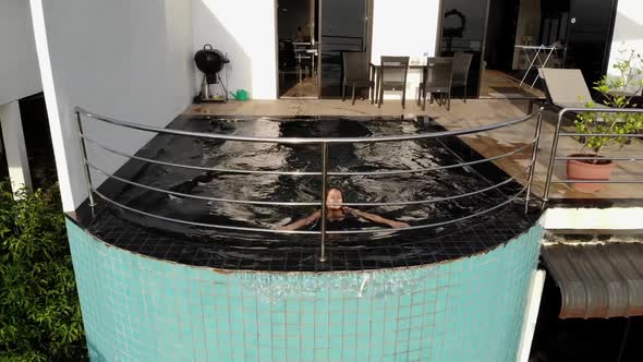 Aerial Top View of Slim Young Woman in Black Bikini Relaxing in Swimming Pool on Tropic Garden Villa