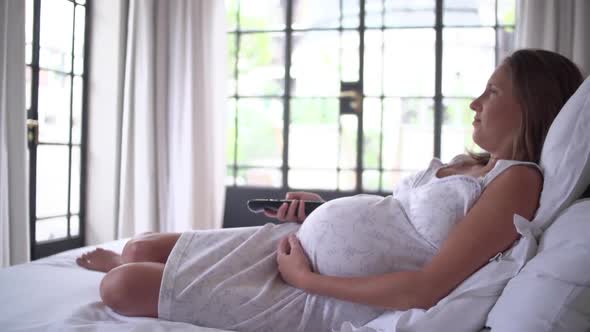 Pregnant woman resting on bed, watching TV