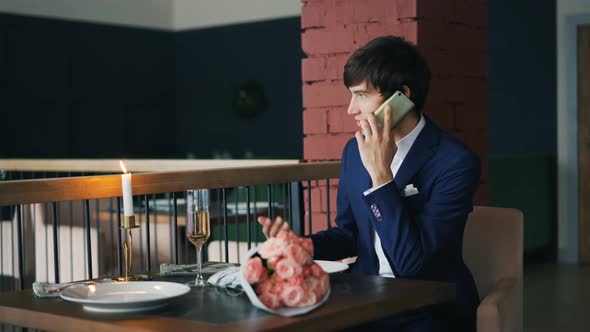 Upset Guy Is Talking To His Girlfriend on Mobile Phone Sitting at Restaurant Alone and Waiting 