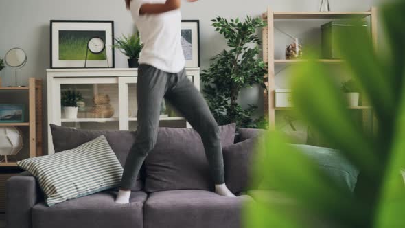 Playful African American Woman Is Jumping Dancing on Couch at Home Listening To Music with