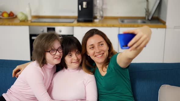 Woman Taking a Selfie with Her Daughters with Down Syndrome Sitting on the Sofa in the Living Room