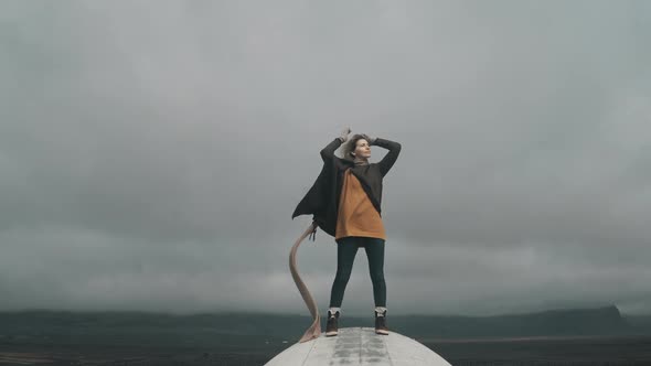 Freedom: Young Blonde Woman Standing on the Top of Crashed DC-3 Plane in Iceland and Raising Hands