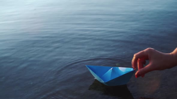 Paper ship in children hand. Blue paper ship. Beautiful sunset