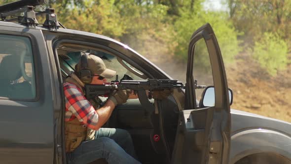 Caucasian Male in Cap Plaid Shirt and Sunglasses Firing Airsoft Gun Sitting on Car Seat