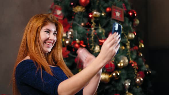 Woman Next To Christmas Tree Uses Smartphone To Communicate Remotely.