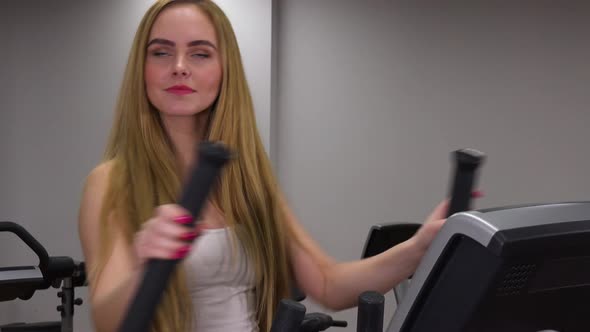 A Young Beautiful Woman Trains on an Elliptical Trainer in a Gym - Closeup