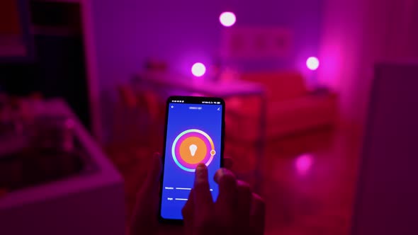 Woman Changing Color of the Lights with Smart Home App on Her Smartphone. Smart Home House Concept. 