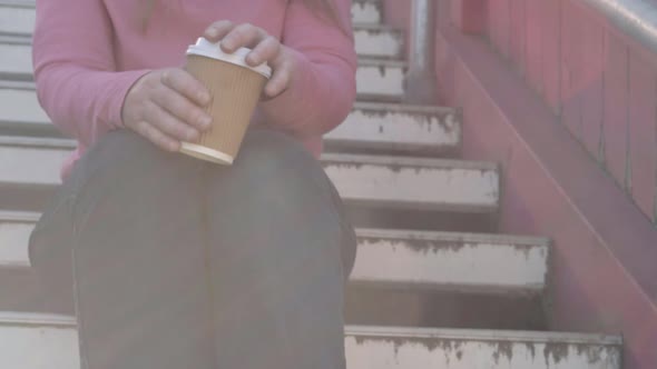 Woman sitting on steps drinking take out coffee medium shot