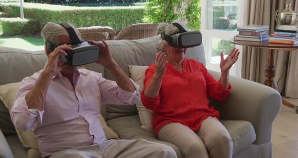 Caucasian senior couple sitting on couch in living room using vr headsets