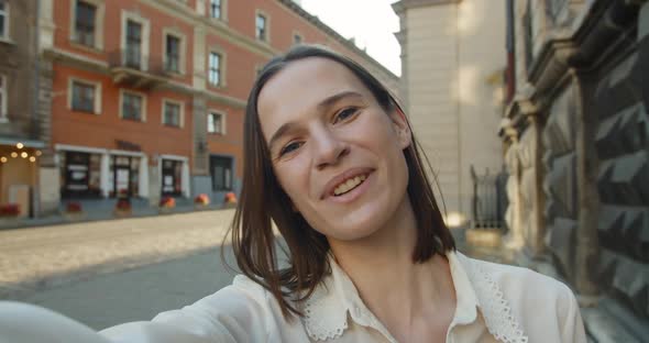 Joyful Young Woman Waving and Talking While Having Video Conversation at Street. Millennial Girl